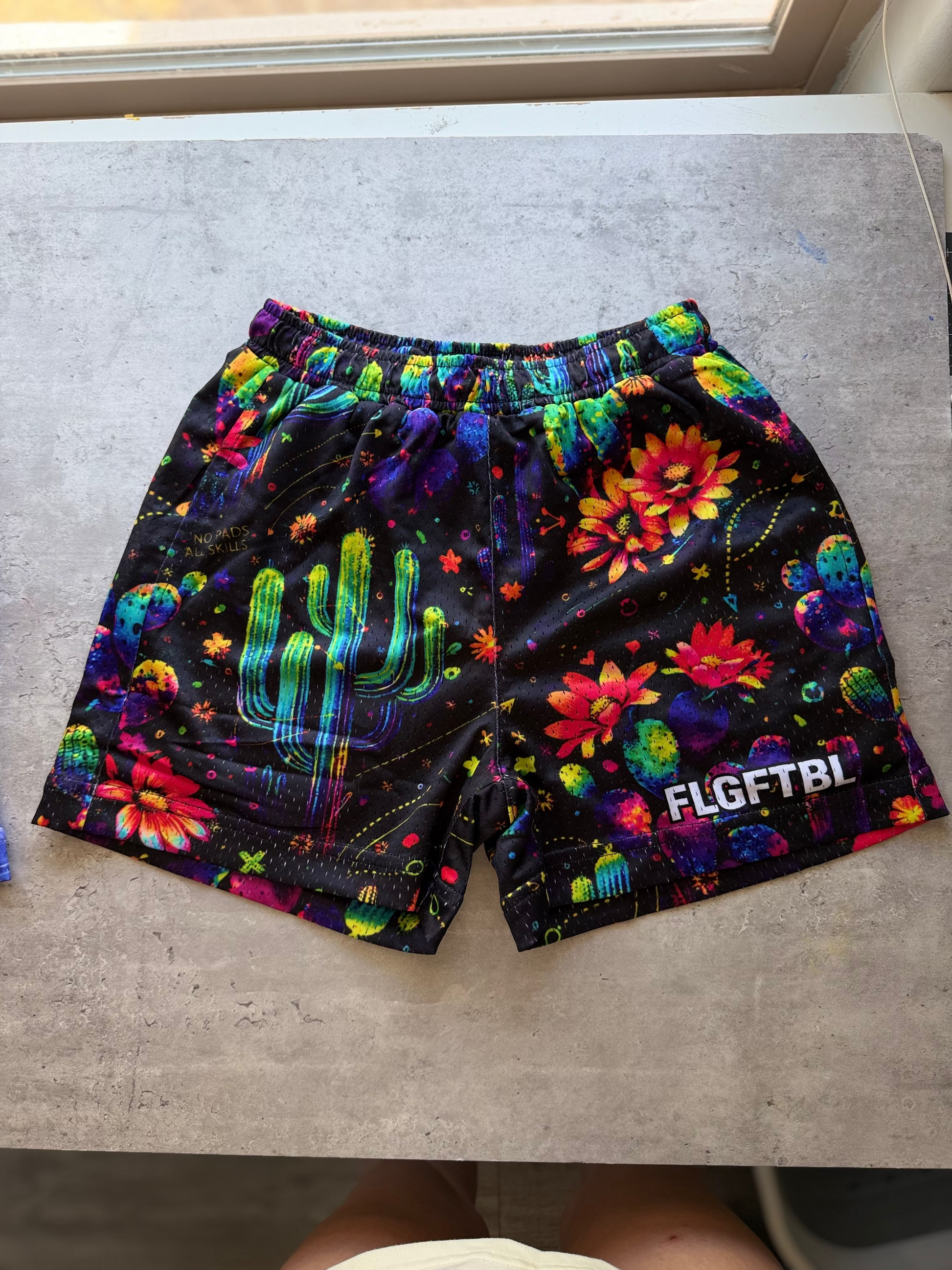 Colorful floral-patterned shorts with FLGFTBI branding on a concrete floor.